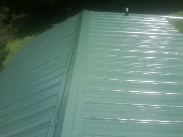 New green metal panels meeting at the ridge of a roof — Flat Roof Repair work by our crew in Dumont