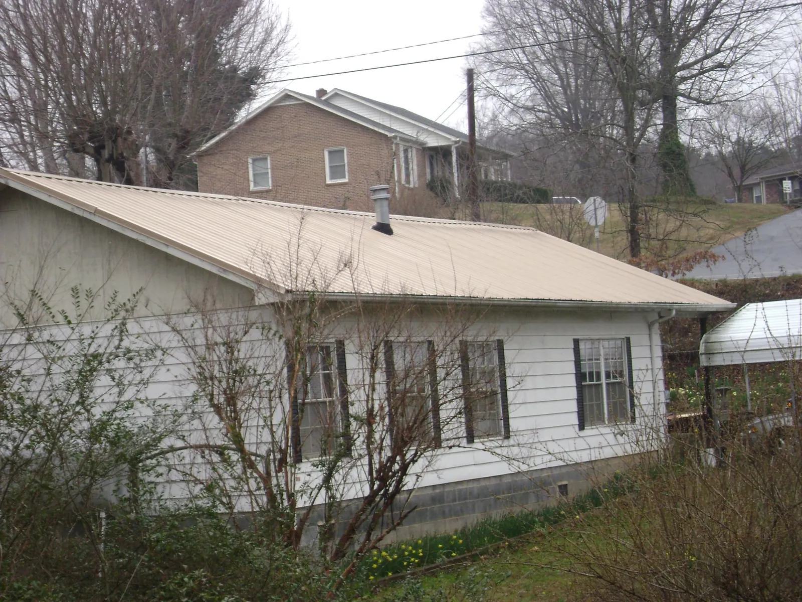 Tan metal roof on a white sided house set into a hillside — Commercial Roofing by Roofing Brothers in Dumont