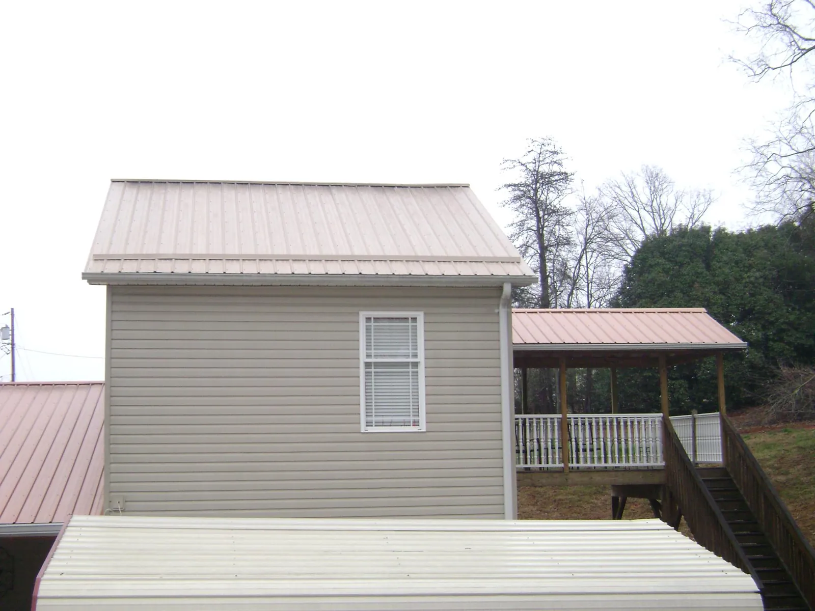 Tan metal roofs on a two story addition and attached porch, from a Roof Replacement job in Dumont